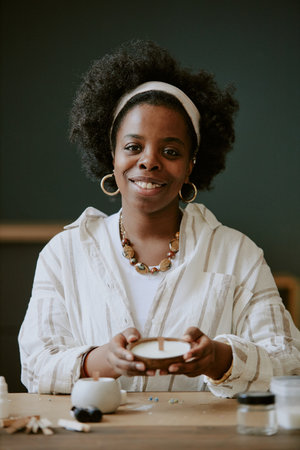 Portrait of African American woman sitting at table and making handmade craft item with a warm...