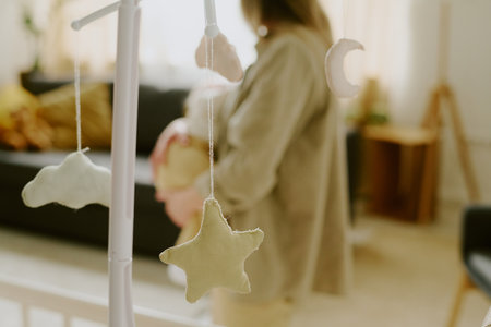Blurry photo capturing woman holding baby in a cozy nursery with a mobile in foreground creating soft, calming ambiance in roomの写真素材