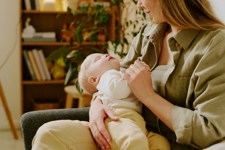 Caring mother tenderly holding sleeping baby in cozy home setting with plants and bookshelf in...