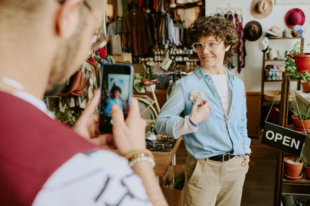 Woman with curly hair smiling while holding handmade item in artisan shop filled with various crafted goodsの写真素材