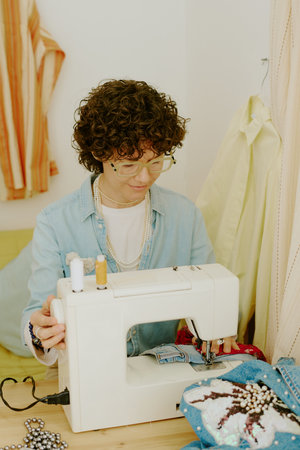 Caucasian person focusing on intricate sewing task with a modern sewing machine surrounded by...