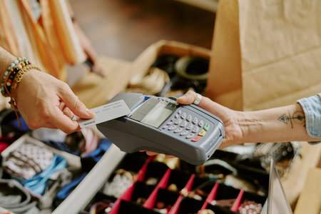 Hand holding payment card while completing transaction through point-of-sale device in retail...