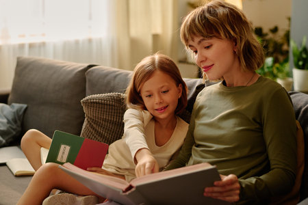 Little girl sitting next to her mom and reading book together