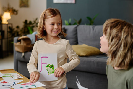 Smiling girl holding paper card with frog and English letter while her mom teaching her pronunciationの写真素材