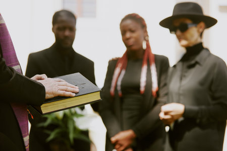 Unrecognizable pastors hands holding black leather bible while biracial family bewailing their loss