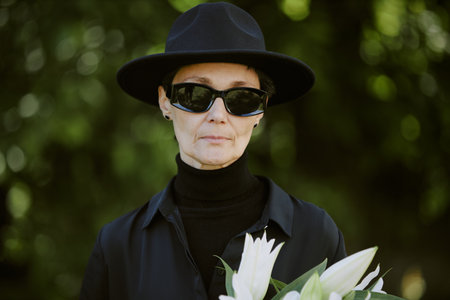 Mourning widow holding bouquet during burial service, she hiding her tears under sunglassesの写真素材