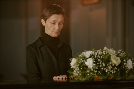 Senior mourning widow touching black coffin as goodbye gesture
