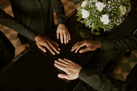 High angle shot of unrecognizable biracial hands on coffin next to bouquet of white rosesの写真素材