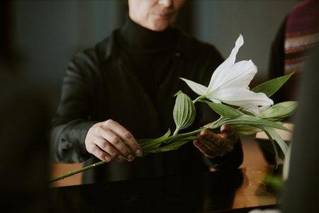Unrecognizable senior woman dressed in total black laying madonna lily on black coffinの写真素材
