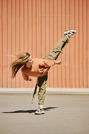 Dancer captured mid-air while performing dynamic move with hair flowing, against bright orange wall background with clear blue sky suggesting energetic and expressive dance styleの写真素材