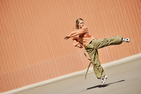 Person performing a dynamic dance move while wearing casual clothing in urban setting. Background features corrugated metal wall, adding texture to sceneの写真素材