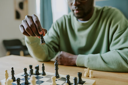 Medium closeup of young African American man sitting at wooden table solving chess problemの写真素材