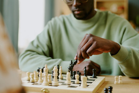 Hand of young African American man moving queen piece during chess game with unrecognizable friendの写真素材