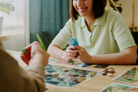 Cheerful young woman holding cards smiling while playing modern thematic board game with her friendの写真素材