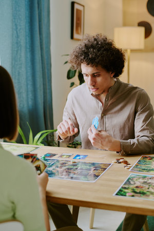 Vertical over shoulder shot of young biracial man and his girlfriend spending spare time at home playing board gameの写真素材