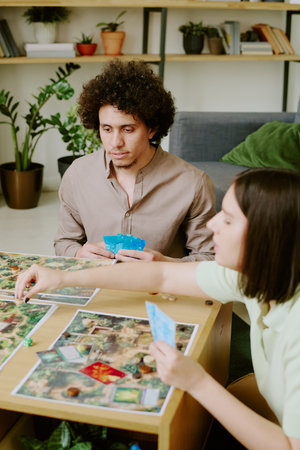 Vertical high angle view shot of ethnically diverse couple spending free time playing roll-and-move board gameの写真素材