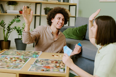 Cheerful young biracial couple doing high five while playing modern fantasy board game in living room at homeの写真素材