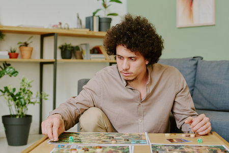 Medium shot of young gen Y biracial man sitting at coffee table in living room at home and playing modern board gameの写真素材