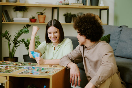 Cheerful young Caucasian woman sitting at coffee table playing board game with her boyfriend and...