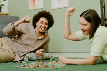 Cheerful young ethnically diverse couple having fun playing board game on floor in living roomの写真素材
