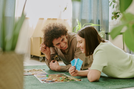 Happy young biracial couple playing modern board game while relaxing on floor in cozy living room at...