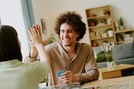 Over shoulder shot of unrecognizable girl doing high five with her joyful boyfriend while playing thematic board gameの写真素材