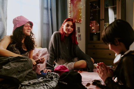 Group of friends enjoying casual time in a cozy bedroom, surrounded by soft pillows and colorful decor, engaging in conversation and activities togetherの写真素材