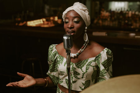 Medium shot of young African American woman singing jazz song on stage in bar late in eveningの写真素材