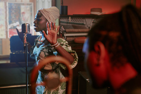 Selective focus shot of young Black woman singing jazz song in microphone during rehearsal with bandの写真素材