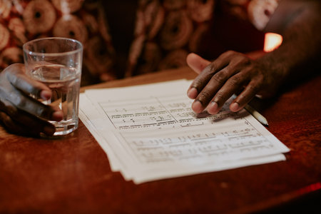 Closeup of unrecognizable African American musician sitting in bar with sheet music on wooden tableの写真素材