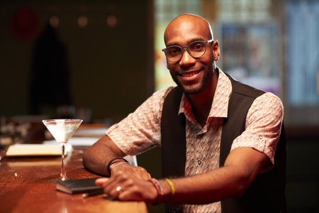 Medium portrait of cheerful young African American man spending evening in local bar smiling at cameraの写真素材