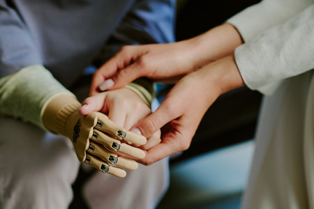 Person gently holding metal prosthetic hand, providing emotional and physical support, highlighting human connection with technology, illustrating acceptance of advanced prostheticsの写真素材