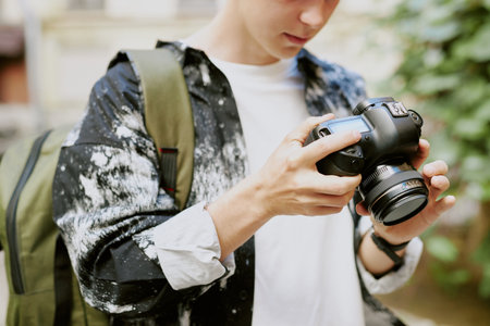 Close-up of a photographer adjusting settings on a camera while wearing a backpack in an outdoor setting. Focused on camera screen with greenery in backgroundの写真素材