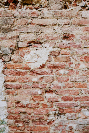 Detail of an aged brick wall with cracked, peeling plaster revealing underlying red and white bricks. The texture of the wall shows signs of erosion and structural wearの写真素材