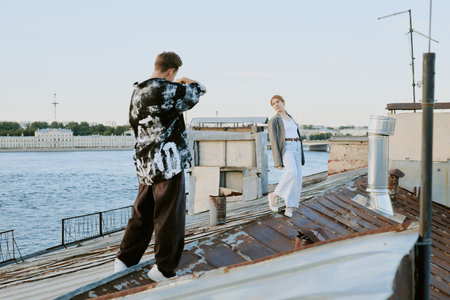 Two people standing on rooftop near river, engaged in taking photographs with scenic cityscape in background and modern urban setting around themの写真素材