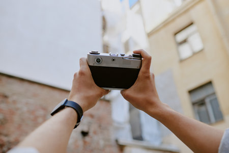 Close-up view of hands holding vintage camera while capturing urban architecture surroundings. Watch...