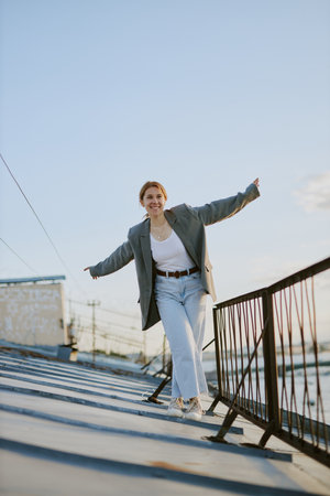 Woman enjoying walk on rooftop basking in daylight with arms outstretched and smile on face showing relaxed and happy moodの写真素材