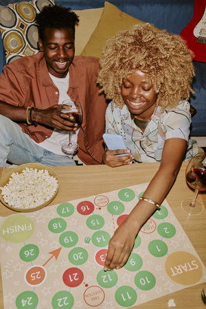 High angle shot of friends playing board game while drinking wine