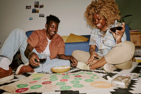 Old friends sitting on soft carpet, drinking red wine and playing board game together