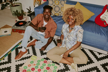 High angle shot of young couple sitting on floor and posing for photo while drinking wine
