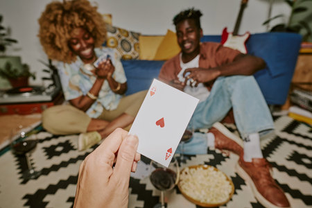 Medium close up of unrecognizable male hand holding heart ace, friends holding card and having fun in blurred backgroundの写真素材