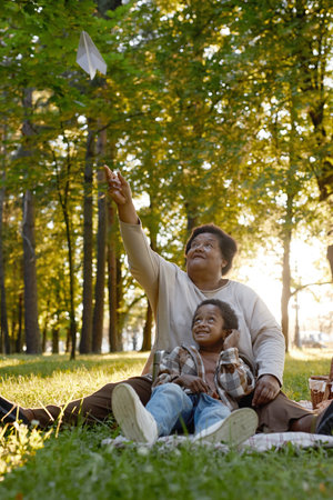 Vertical shot of African American family admiring paper airplane, they having picnic in parkの写真素材