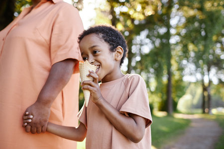 Low angle shot of African American boy enjoying ice cream while spending weekend with grandmother in parkの写真素材