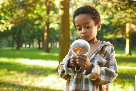African American boy holding chanterelle and loupe while examining it in forestの写真素材