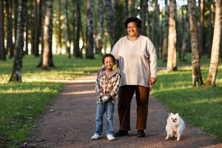 Portrait of African American granny and her grandson walking with snow white spits in green parkの写真素材