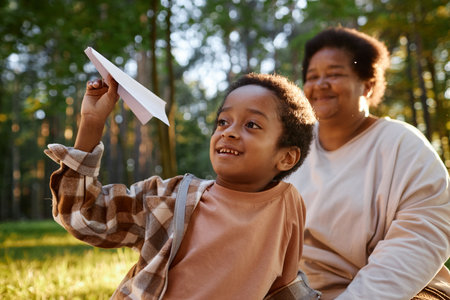 Medium close up of African American boy flying paper airplane while his grandmother admiring himの写真素材