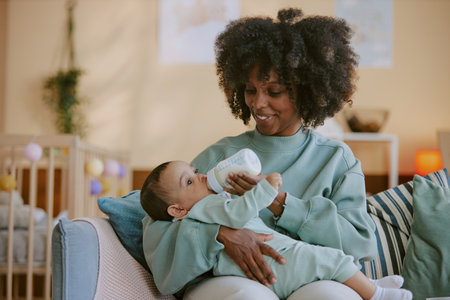 African American mother holding her son and feeding him while he looking around nursery and eating