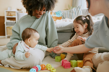 Baby boy touching hands of Asian girl and her mother while his African American mom watching them and smilingの写真素材