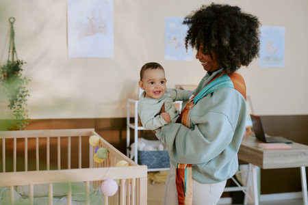 Smiling African American mother holding her curious and lovely baby in slingの写真素材