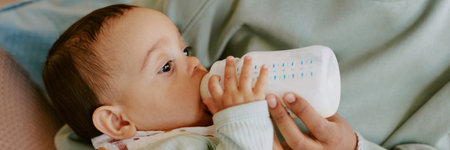 Website banner of unrecognizable mothers hand holding baby bottle with kids formula while feeding her baby boyの写真素材